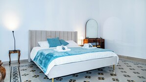 A neatly made bed with a blue blanket, a bedside table with a lamp, and a mirror on the wall.