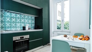 A modern kitchen with green cabinets, a Bosch oven, and a dining area with a table set for breakfast.