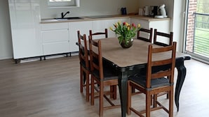 Comedor con una mesa y sillas de madera, una araña y vistas al exterior a través de una ventana.