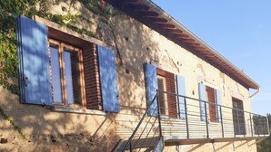 Un edificio de piedra con una escalera que conduce a un balcón, con contraventanas de madera en las ventanas.