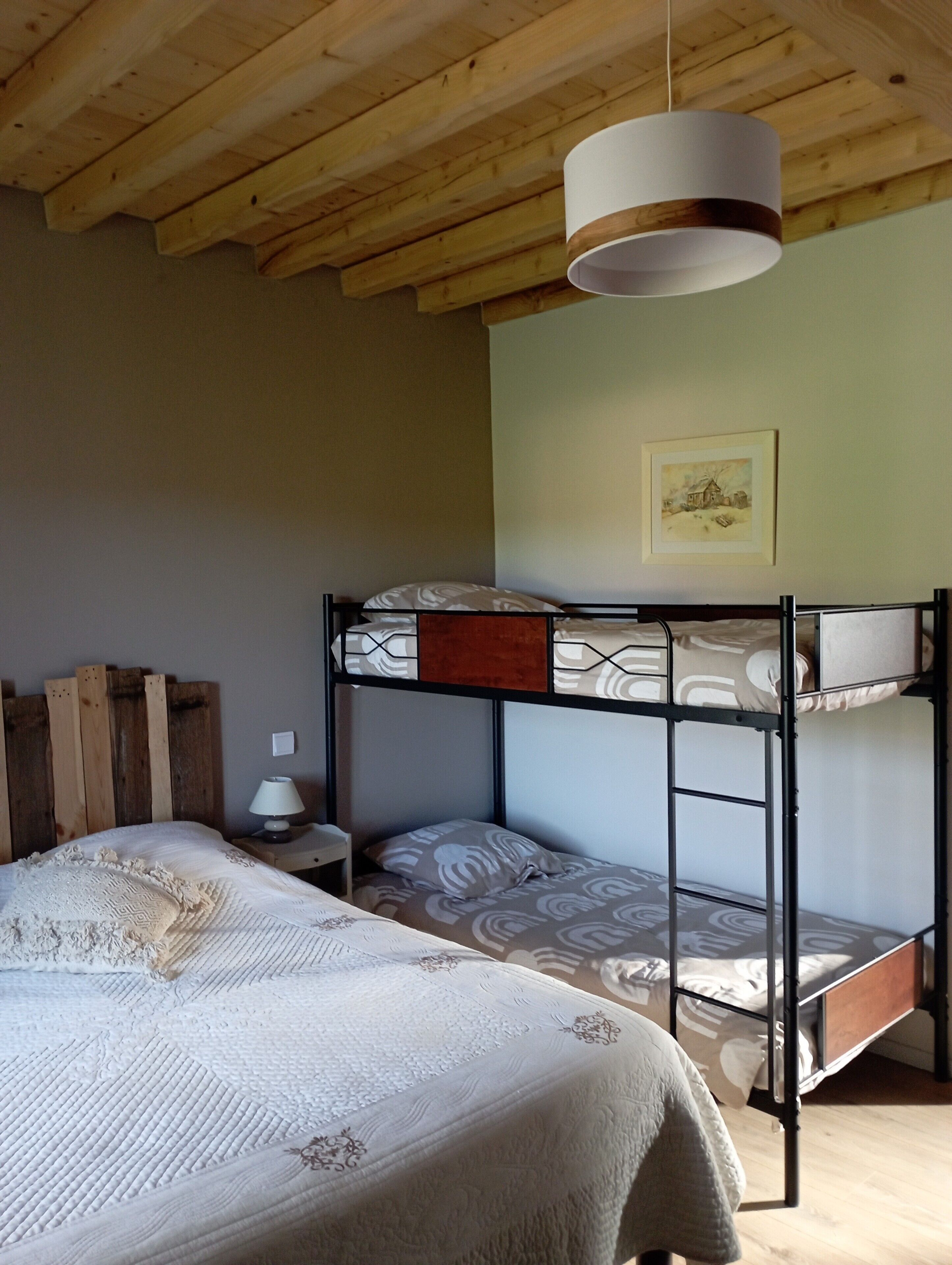 Un lit superposé avec une tête de lit en bois, une table de chevet avec une lampe et un tableau encadré accroché au mur.