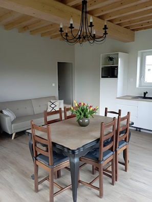 En matplats med ett träbord, stolar, en kristallkrona, en soffa och ett kök i bakgrunden.