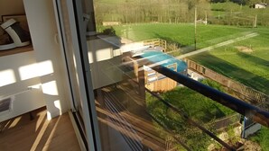 A balcony with a view of a swimming pool, grassy area, and distant hills.