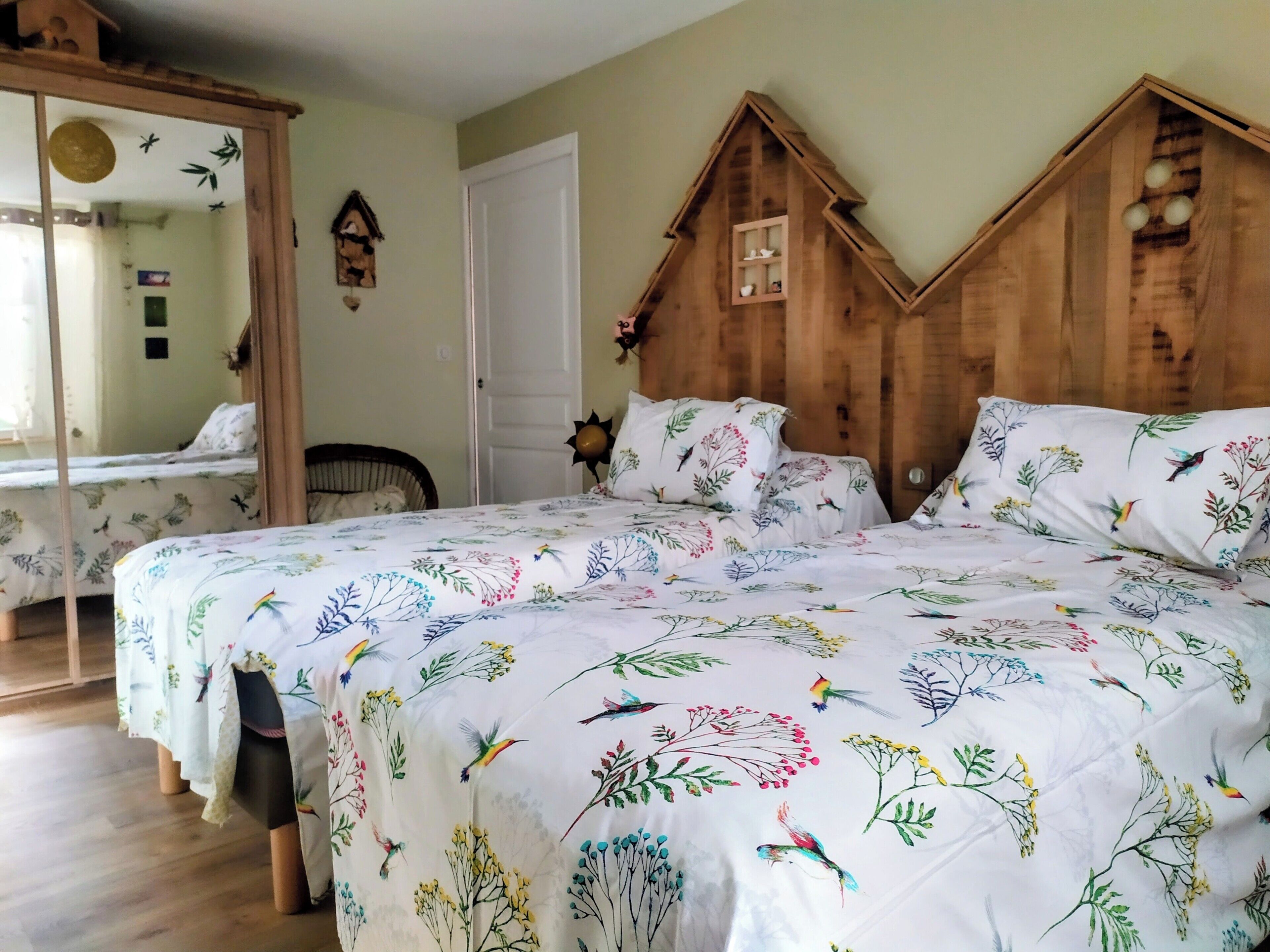 A bedroom with a large bed, a wooden headboard, a mirror, and a wall-mounted birdhouse.
