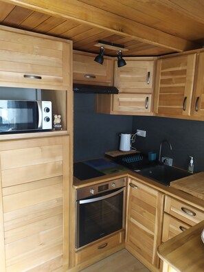 Une cuisine compacte avec des meubles en bois, un four à micro-ondes, un four traditionnel, un évier et un plan de travail noir.