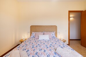 Une chambre à coucher avec un lit, deux tables de chevet avec des lampes, une porte et un luminaire fixé au mur.