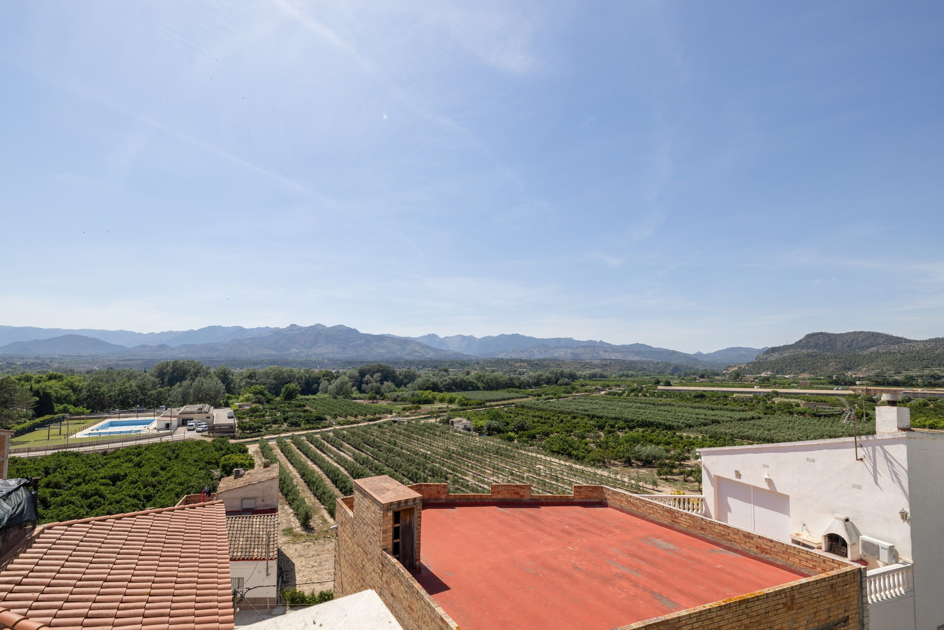 A rooftop terrace with a red roof, overlooking a vineyard and distant mountains.