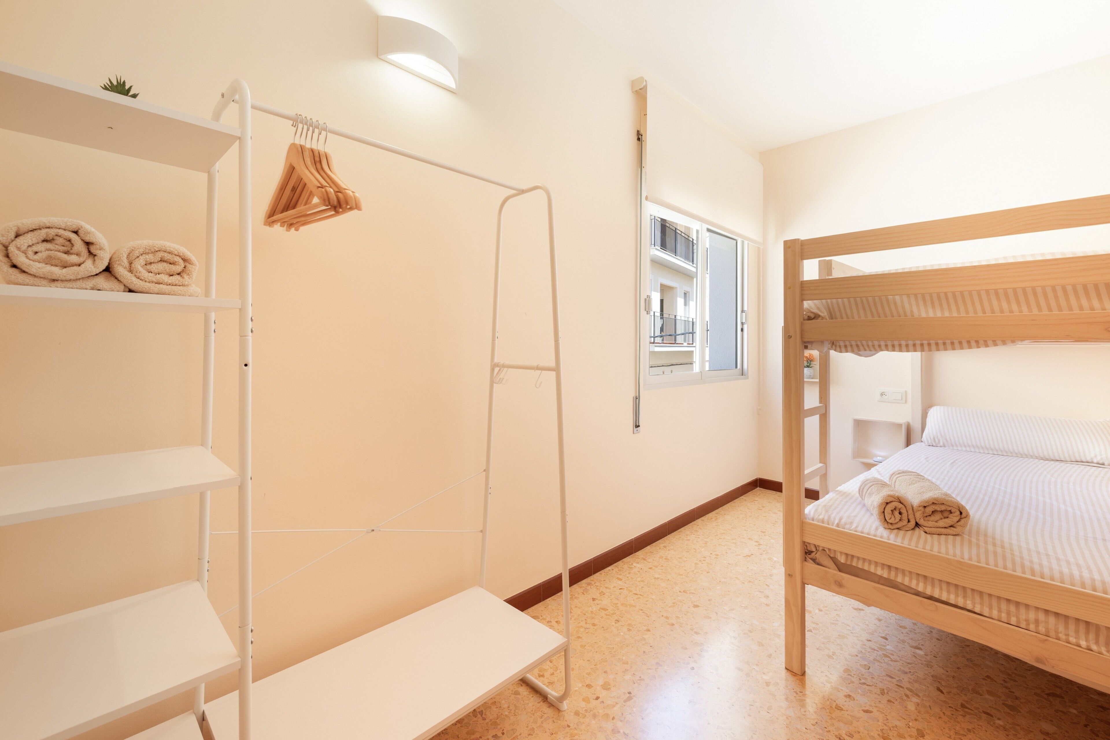 Una habitación con literas, un estante blanco con toallas, una escalera y una ventana con vistas al balcón.