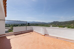 Une terrasse sur le toit offrant une vue dégagée sur les montagnes lointaines, avec une balustrade blanche et un sol en briques.