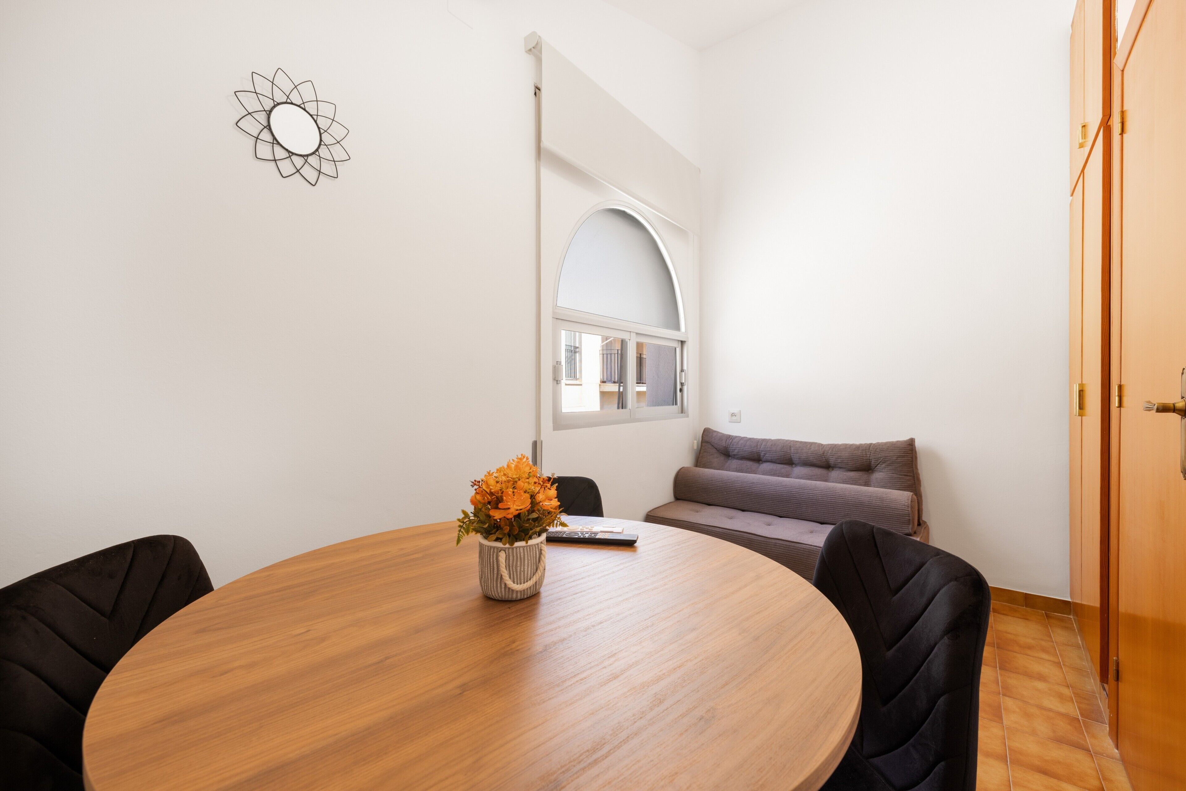 A room with a round wooden table, a sofa, and a window with an arched design.