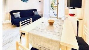 A dining area with a table, chairs, a chandelier, a black sofa, and a TV. - Hostdomus - Cozy corner near the sea (Finale Ligure)