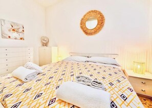 Una habitación de hotel con cama, un espejo redondo, una lámpara de noche y una obra de arte colgada en la pared.