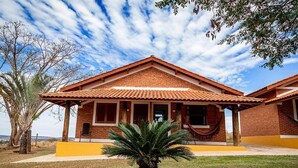 Un edificio de dos pisos con fachada de ladrillo, techo de tejas y un pequeño jardín delantero con una palmera.