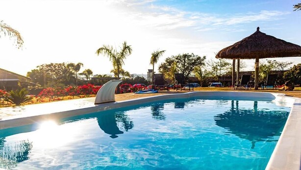 Una piscina con borde curvo, rodeada de sillas de descanso y un paraguas de paja.