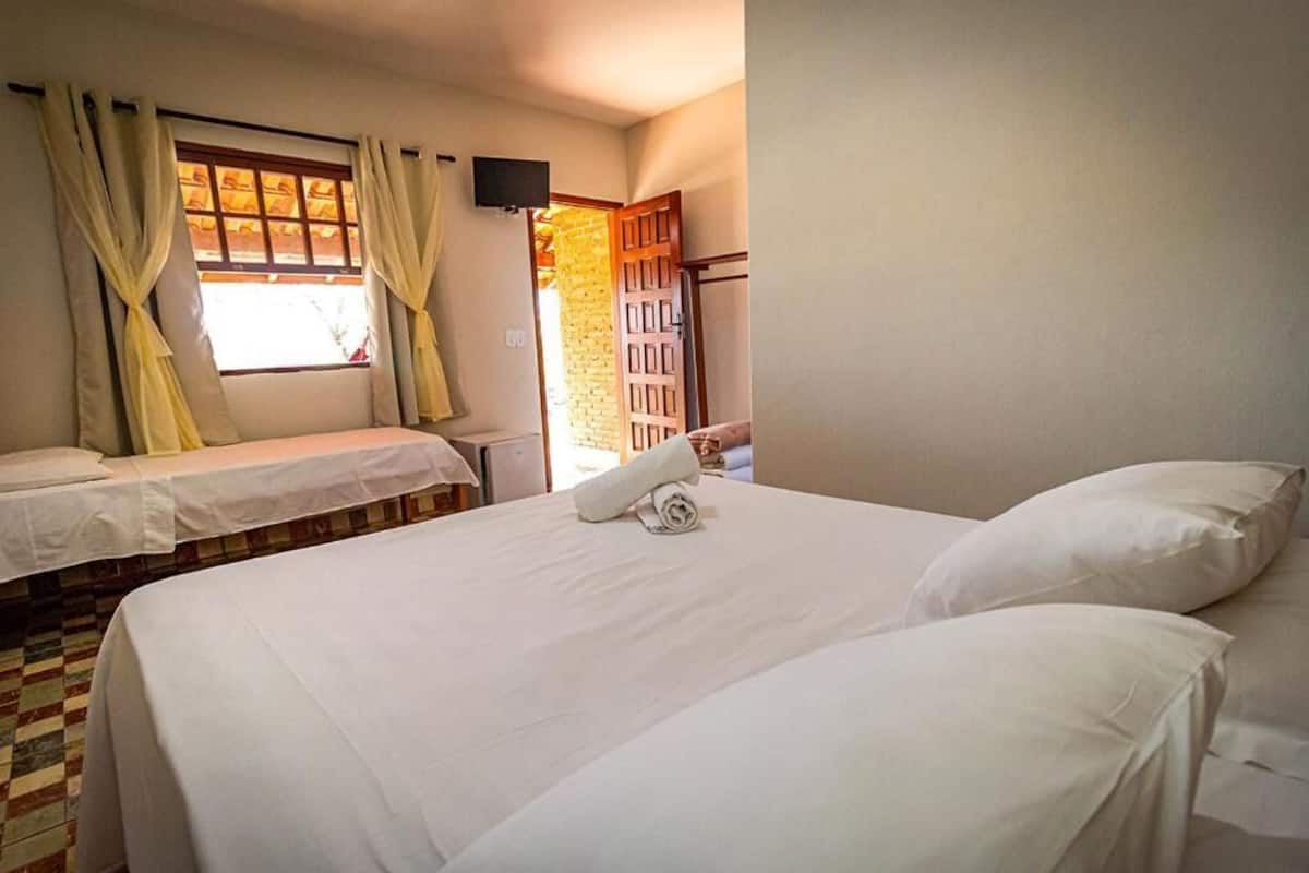 Habitación de hotel con dos camas, una ventana con cortinas, un televisor en la pared y una puerta que da a un muro de ladrillo.