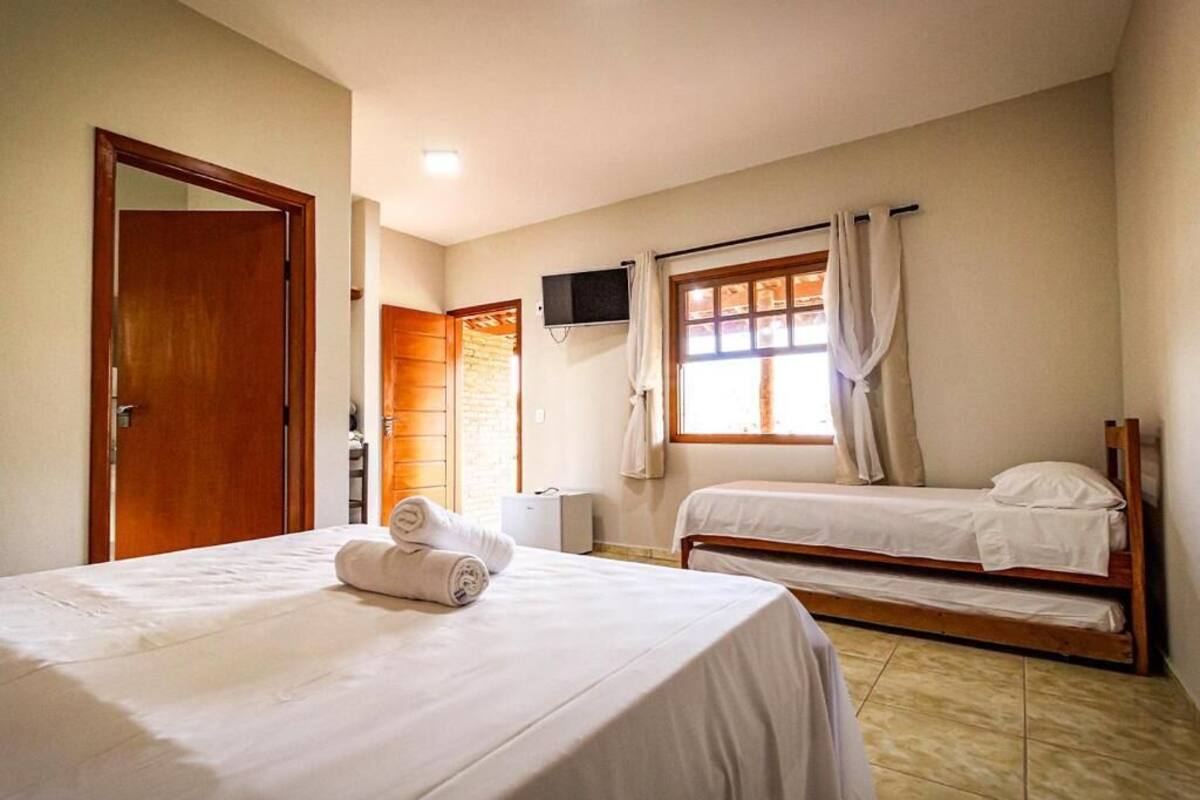 Habitación de hotel con una cama, una cama individual, un televisor, una ventana con cortinas y una puerta.