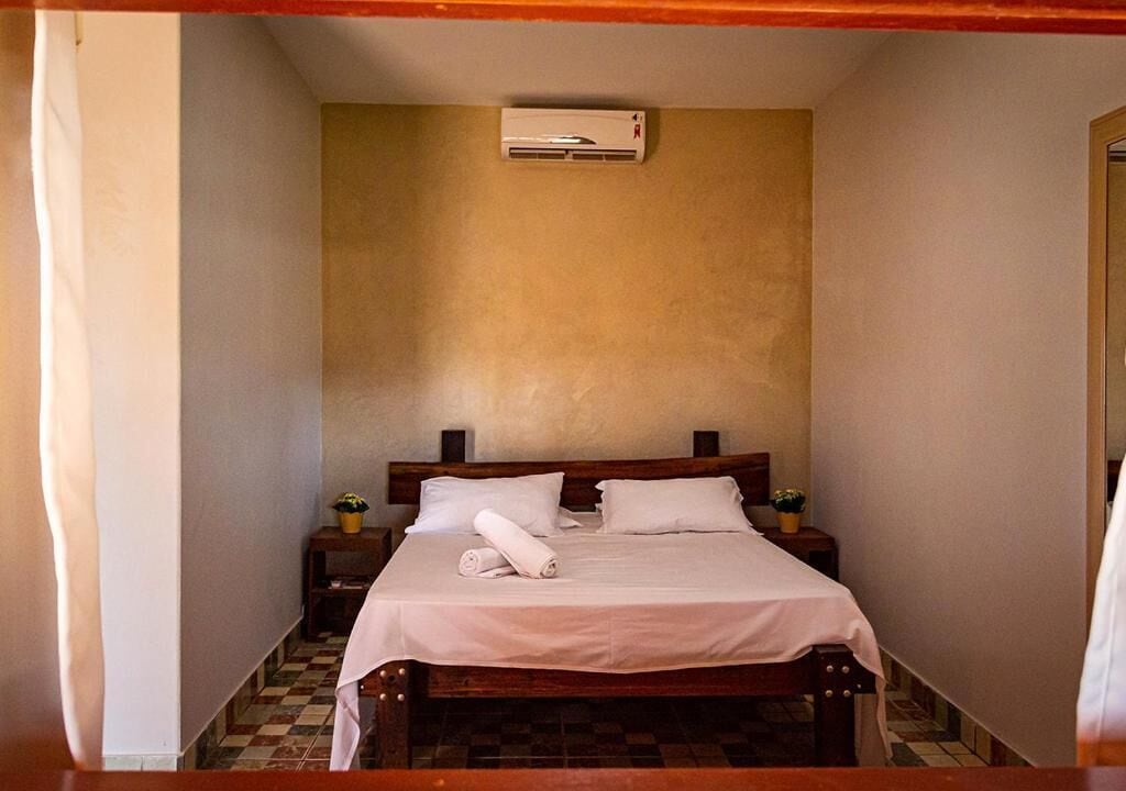A bedroom with a bed, a nightstand, a wall-mounted air conditioner, and a small table with a plant.