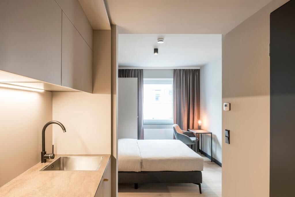 Una habitación de hotel moderna con kitchenette, una cama, un escritorio y vistas a la ciudad.