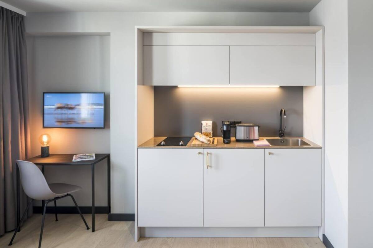 Une cuisine compacte dotée d’un téléviseur à écran plat, d’une petite table avec une chaise et d’un design moderne.