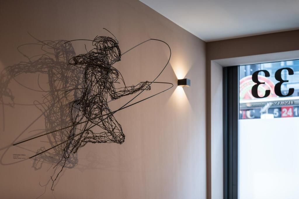 A wire sculpture on a wall, a window with a view of a building, and a wall-mounted light fixture.