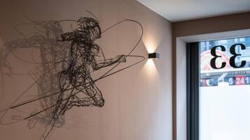 A wire sculpture on a wall, a window with a view of a building, and a wall-mounted light fixture.