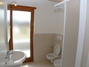 A bathroom with a sink, toilet, and a door leading to another room. - Neat and Quiet Ground-floor Flat Near the sea (San Michele al Tagliamento)