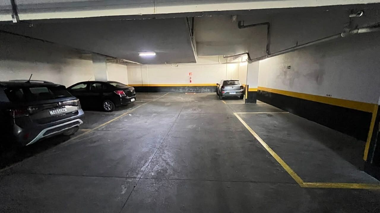A parking garage with three cars parked, concrete floors, and yellow lines marking parking spaces.