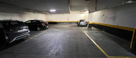 A parking garage with three cars parked, concrete floors, and yellow lines marking parking spaces.