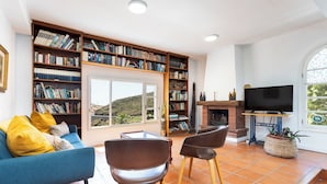 Una sala de estar con un sofá, sillas, una chimenea, un televisor y una amplia estantería.