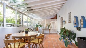 Un patio cubierto con mesa y sillas de madera, plantas en macetas y suelo de baldosas.
