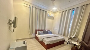 Una habitación de hotel con cama, escritorio, silla, equipo de aire acondicionado y televisor.