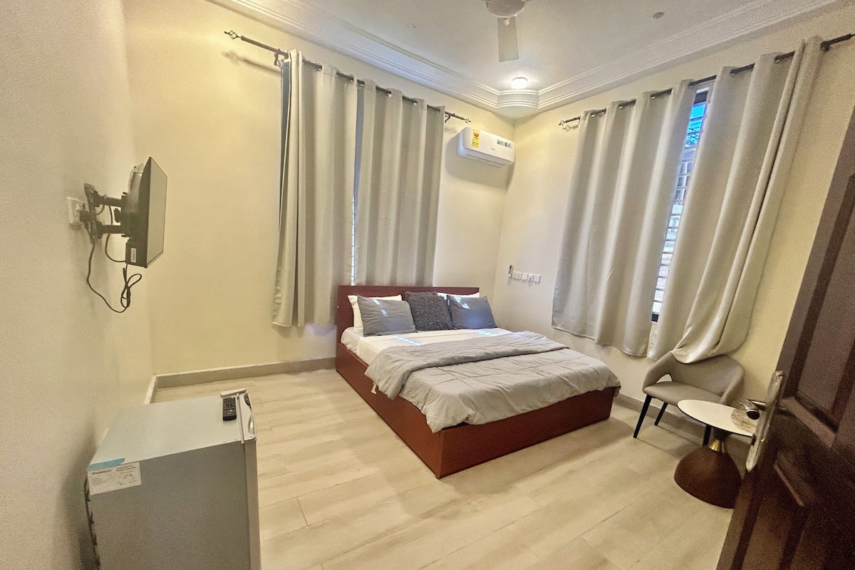 Una habitación de hotel con cama, escritorio, silla, equipo de aire acondicionado y televisor.