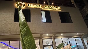 Un edificio con un cartel que dice 'BLISS ESCAPE' y una persona sentada en un banco.