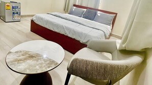 Habitación de hotel con cama, televisión, minibar, una mesita y una silla.