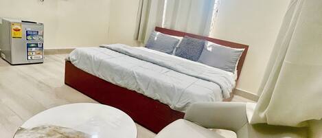Ett hotellrum med en säng, en TV, en minibar, ett litet bord och en stol.