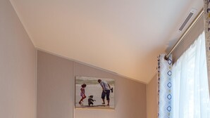 A hotel room with two single beds, a nightstand with a lamp, a painting on the wall, and a window with curtains. - Charming Isle of Wight Holiday Park Retr (Cowes)