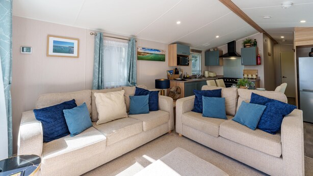 A living room with two sofas, a coffee table, a TV, and a kitchen area with cabinets and appliances. - Charming Isle of Wight Holiday Park Retr (Cowes)