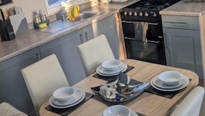 A compact kitchen with grey cabinets, a stove, and a dining area with a table set for four. - Charming Isle of Wight Holiday Park Retr (Cowes)