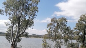 A lakeside view with trees and a clear sky. - Room-bloekombos Guesthouse Family Unit (Kopanong)