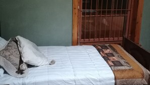 A single bed with a white duvet and patterned pillows, a wooden headboard, a window with a metal grill, and a patterned curtain. - Room-bloekombos Guesthouse Family Unit (Kopanong)