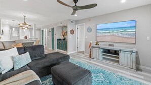 Een moderne woonkamer met een hoekbank, voetenbankje, plafondventilator, televisie en uitzicht op de oceaan.