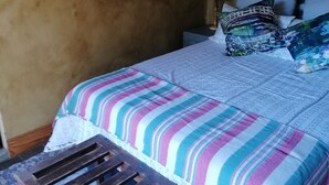 Quarto com cama, mesa de cabeceira, luminária, espelho e um banco de madeira.