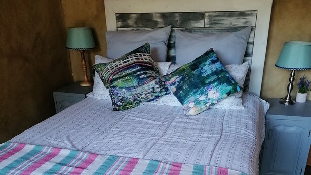 Cama com roupa de cama listrada, almofadas com estampas florais e duas luminárias de cabeceira.