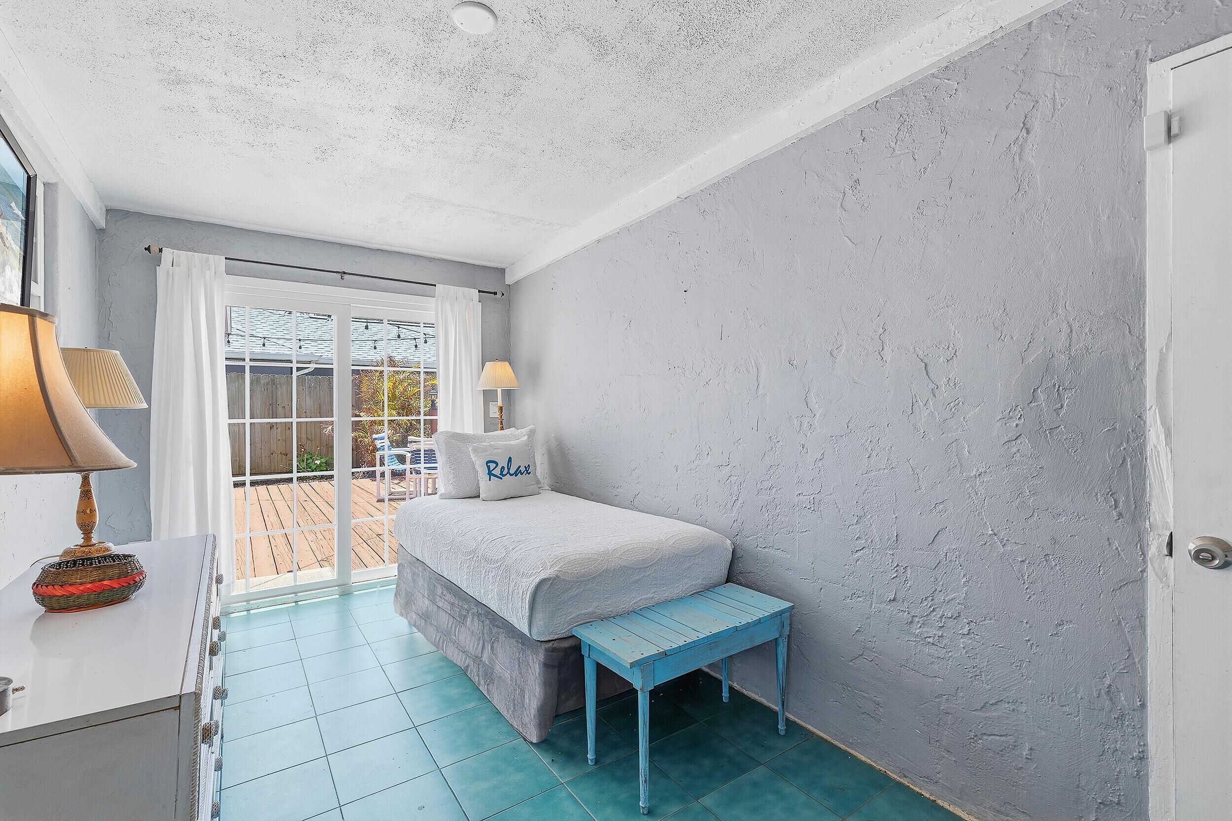 Ein Schlafzimmer mit einem Bett, einer Bank, einer Lampe und Blick durch eine Glastür.