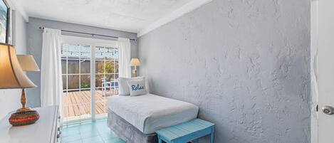 A bedroom with a bed, a bench, a lamp, and a view through a glass door.