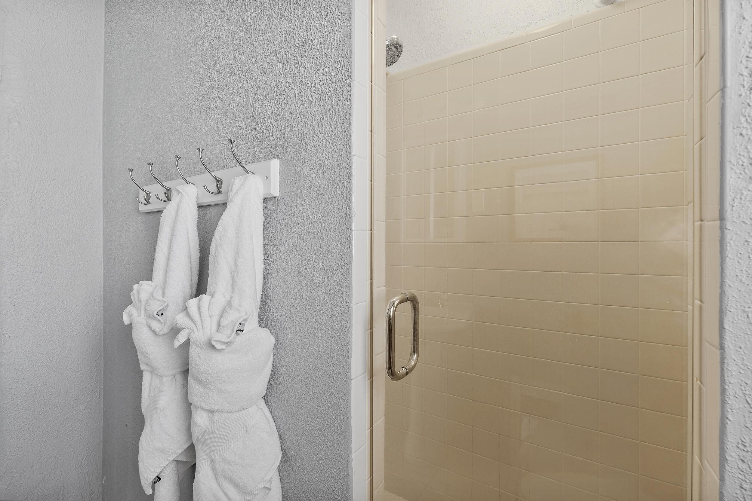 Un baño con zona de ducha, un perchero con toallas y una puerta con manija.