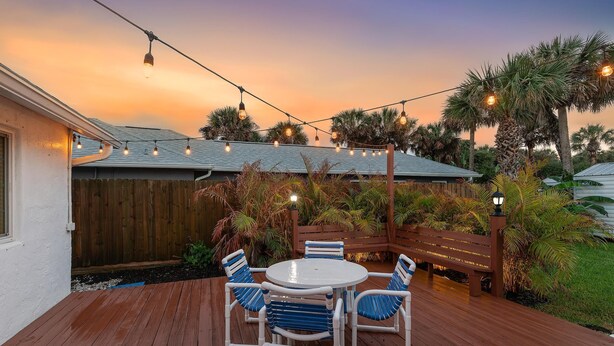 A wooden deck with a round table and chairs, surrounded by a wooden fence and palm trees. - Twenty Palms (New Smyrna Beach)