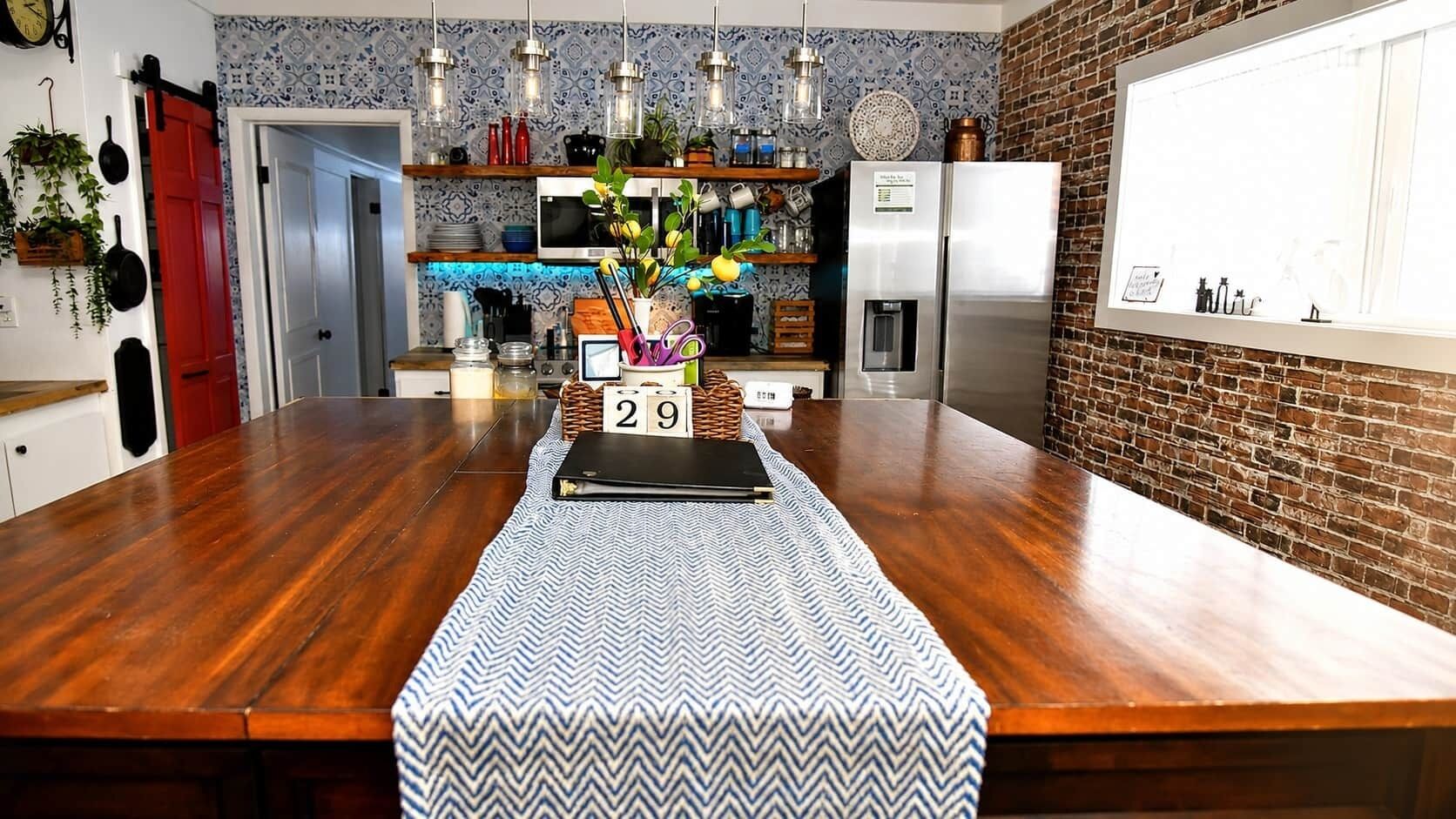 A kitchen with a wooden countertop, a refrigerator, and a backsplash with patterned tiles.