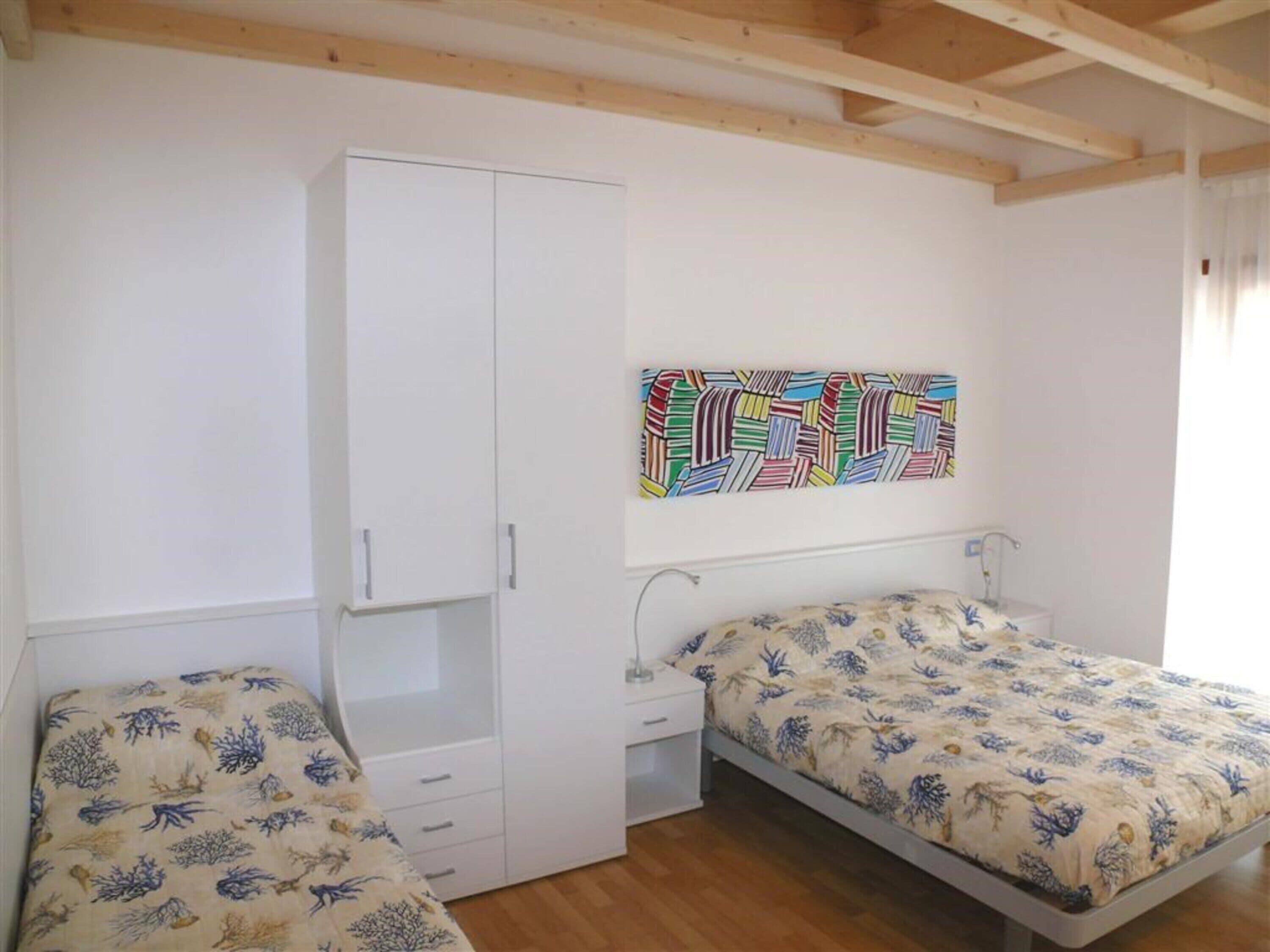A bedroom with two beds, a wardrobe, a nightstand, and a colorful abstract painting on the wall.