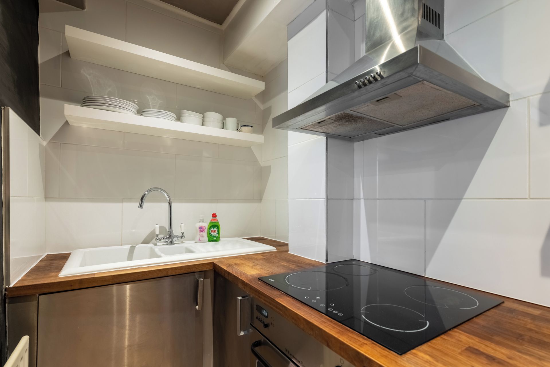 Una cocina moderna con un lavamanos de acero inoxidable, un horno empotrado y una placa de inducción negra.